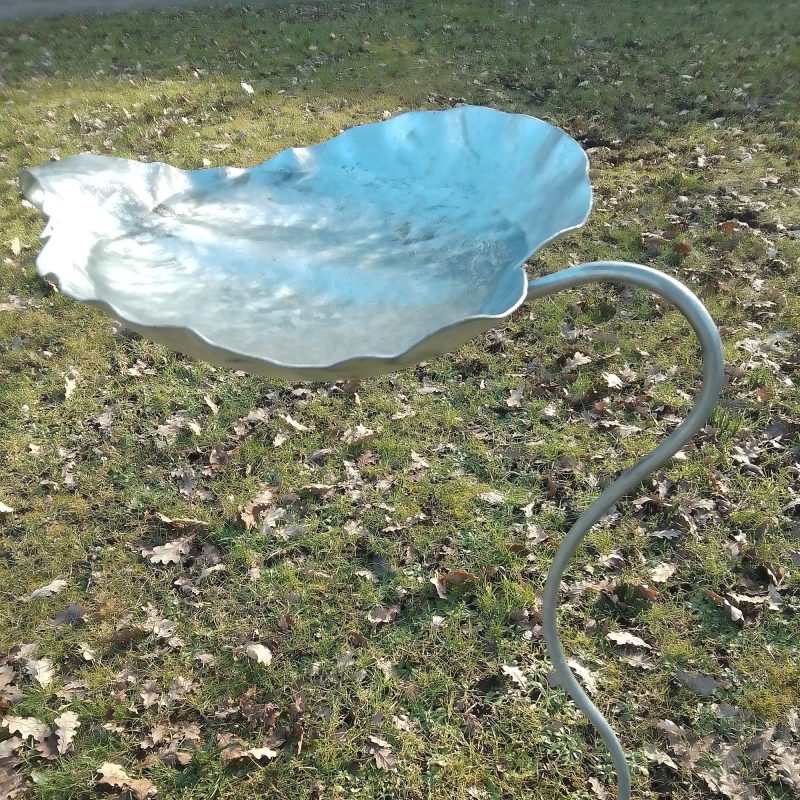A metal bird bath in the shape of a waterlilly leaf.