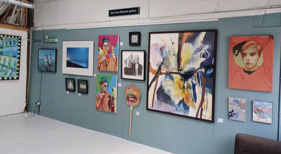 There is a selection of various artwork including painting, prints and photographs hanging on a gallery wall