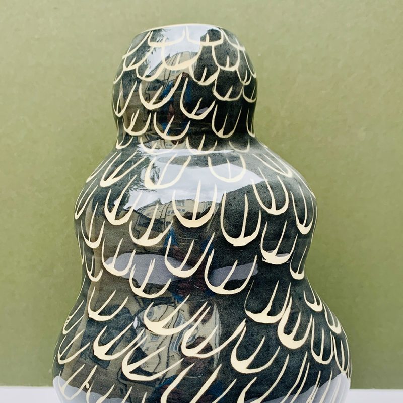 A  curvy ceramic vase with black and white sgraffito feathers.