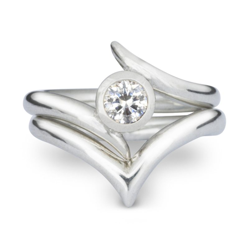 A round diamond in a rubover setting with a spiky surround, in platinum. With a matching fitted v-shaped wishbone wedding ring.