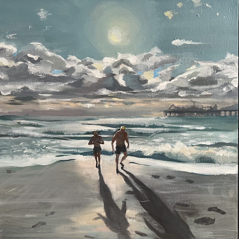 Two swimmers head out from the sea at low tide, it is winter but the sun is low and very bright, casting long shadows