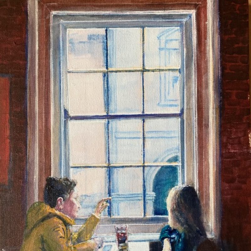 Two people sit at a table in a coffee shop looking out of the window to the street below