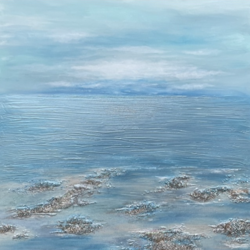 A muted blue seascape with rippling waves, a cloudy blue sky and rock pools in the foreground