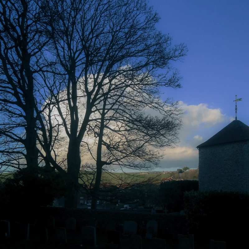 A view of a small Saxon church surrounded by bare trees silhouetted against blue sky