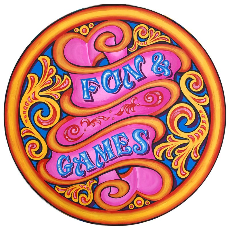 A circular painting in a fairground style of a ribbon with the text 'Fun and Games' and swirls, using bright, bold colours