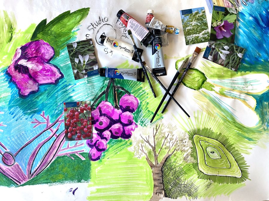 a large sheet of paper covered in colourful images of flowers and foliage.  Several paint brushes and tubes of paint are scattered across the paper