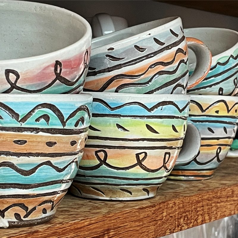Multi-coloured stripey coffee mugs on shelf.