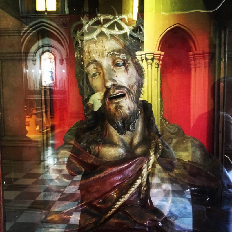 Photograph . A reflection of a man wearing a crown of thorns in what appears to be a church setting.