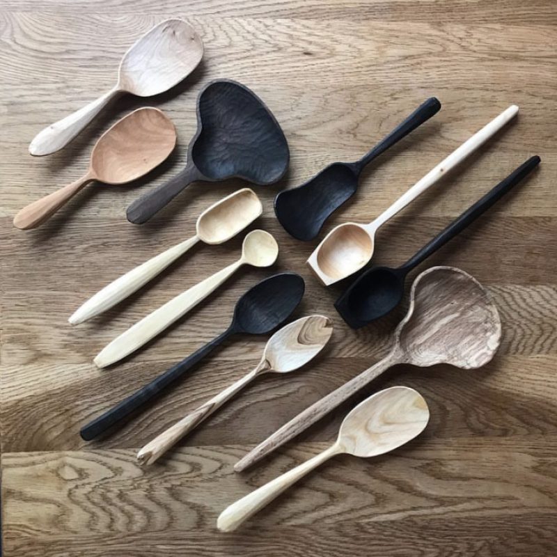 selection of locally sourced woods hand carved in to a variety of spoon shapes laid across a wooden table top.