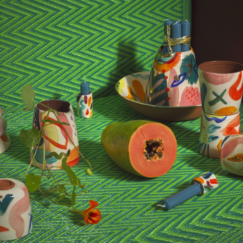 colourful hand thrown terracotta pottery on a green backdrop with flowers and a cut bright orange papaya