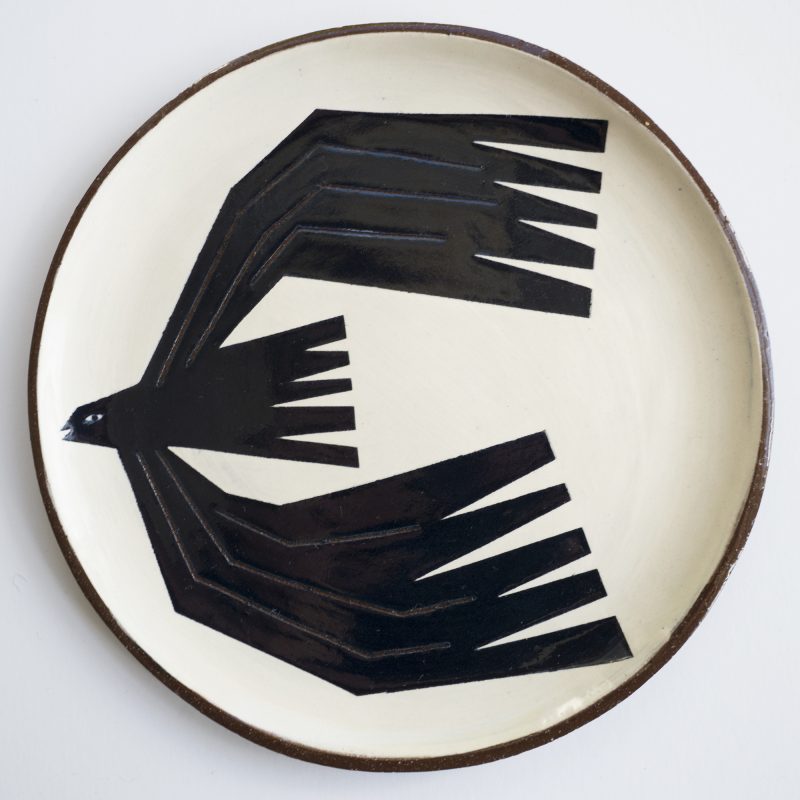 An earthenware clay plate with a graphic image of a rook flying on it