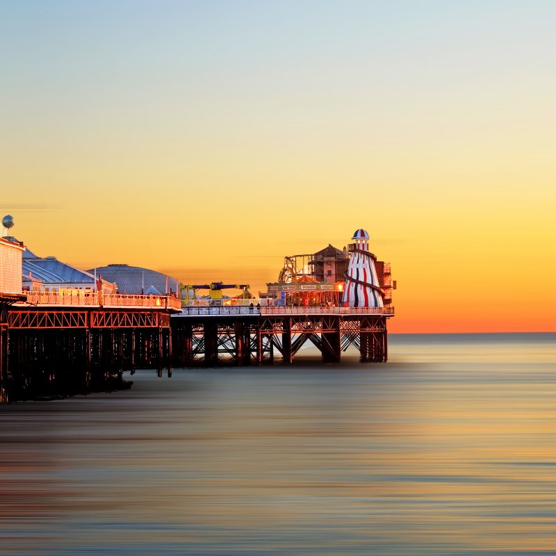 Helter Skelter and Brighton pier at sunset, an orange glow of the sunsetting behind on a still sea