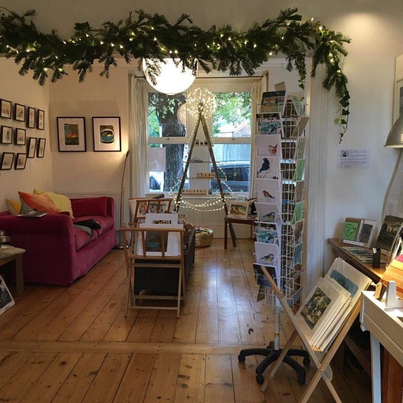 Large through living room with festive garland over the archway, showing a selection of art on the walls, prints in browsers, cards and hand made wooden items