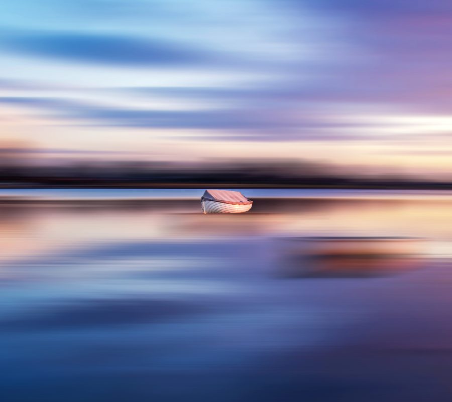 A small rowing boat on calm water, purple, pink and orange glow from the sunset reflecting on the water.