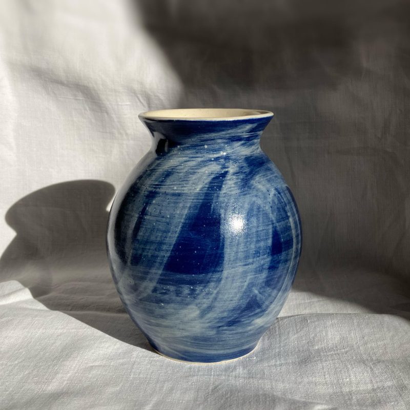 Rounded vase decorated with white brushstrokes against a gloss blue base 