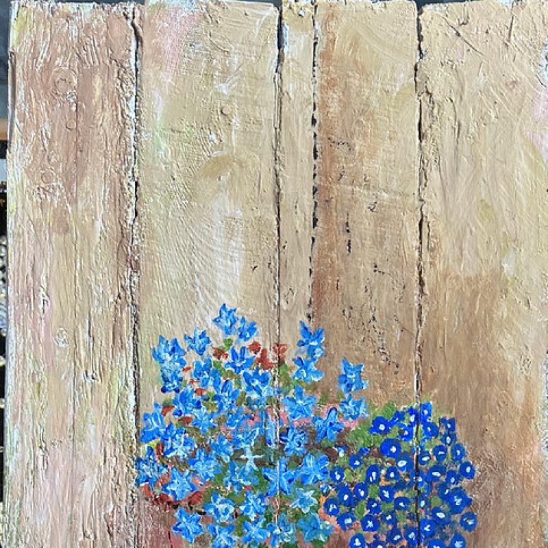 Blue flowers in a pot painted on wooden planks.