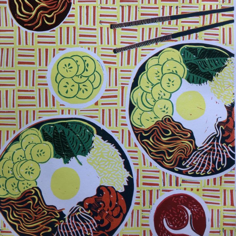 A multi-coloured lino print of  Japanese style plates of food laid out on a patterned cloth from an aerial view.