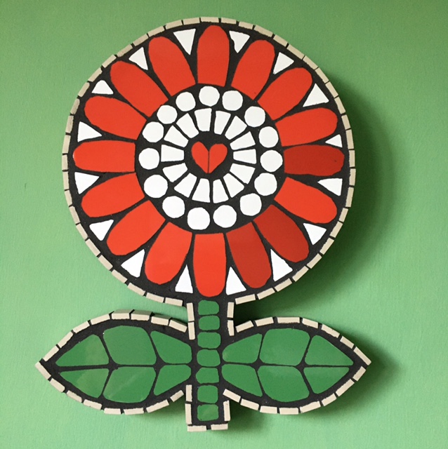 A flower made using mosaic tiles in red on a green background