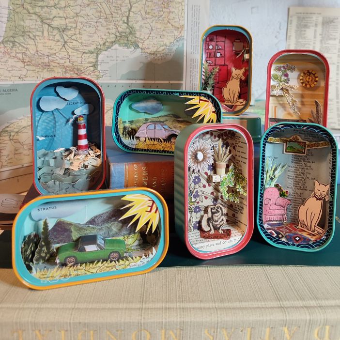 A picture of a collection of quirky dioramas created using vintage maps cut into shapes, housed in little sardine tins.