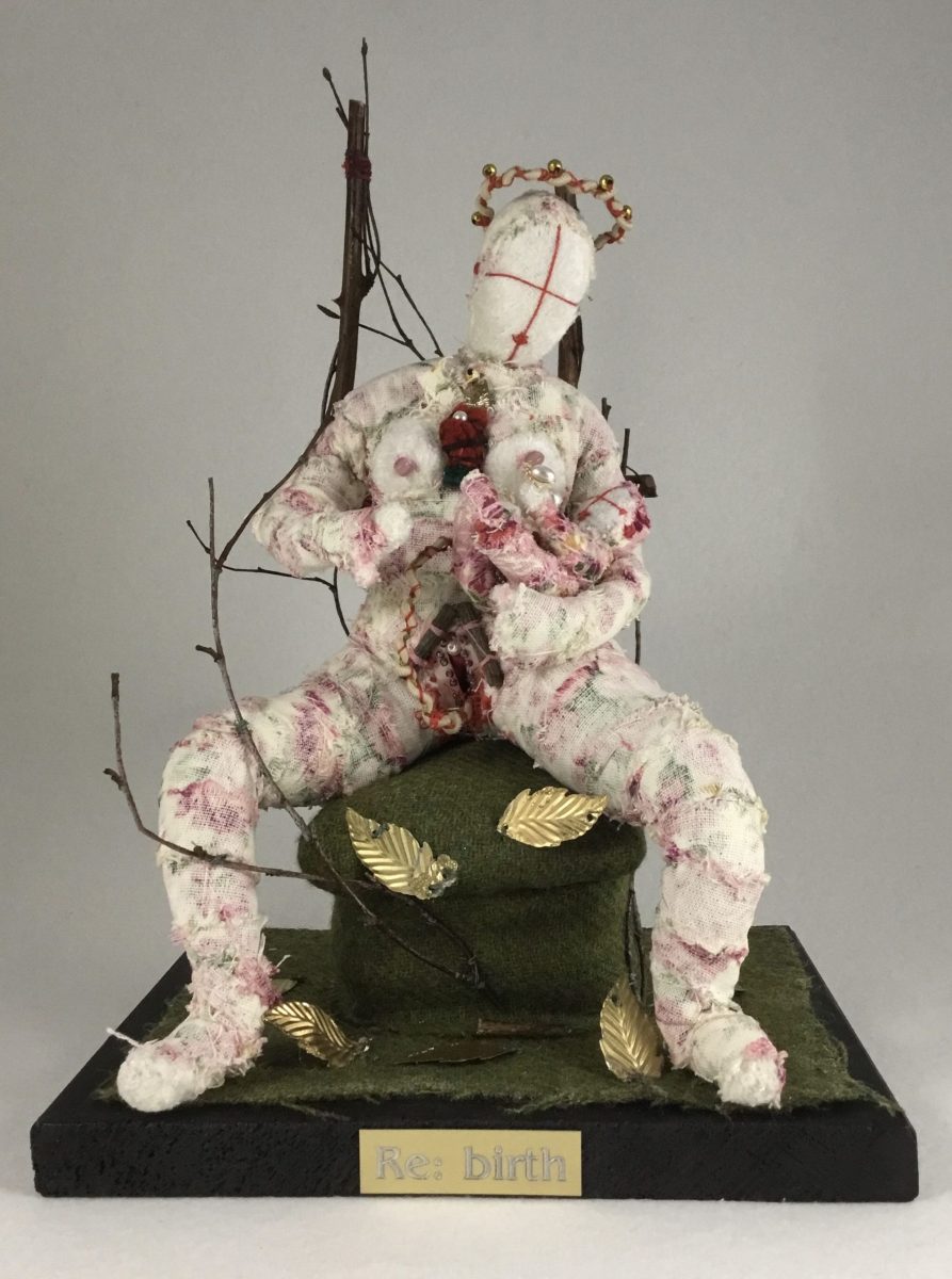 Sculpture of a textile figure holding a baby with branches and a crown