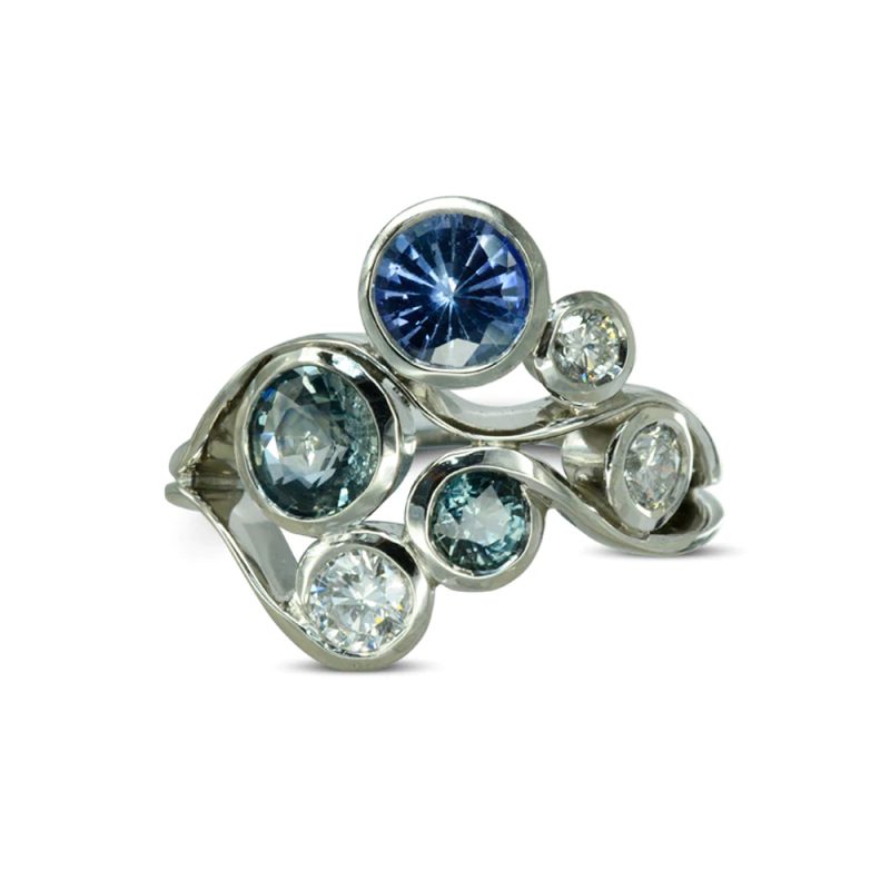 A cluster ring made from varying sizes and shades of sapphires and diamonds wrapped in swirled platinum waves.