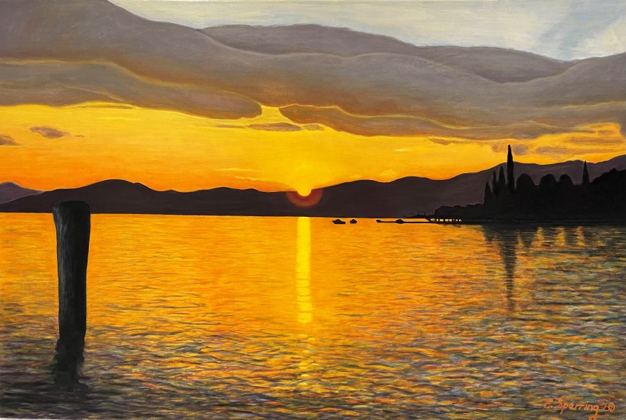 Lake Garda at sunset, a lake scene with mountain backdrop reflections in yellows and oranges.