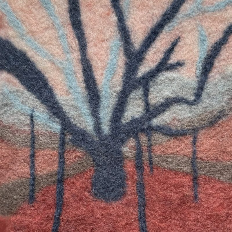 Felted wool image of a mulberry tree with branches held up by stilts. The tree is shades of blue against a pink sky.