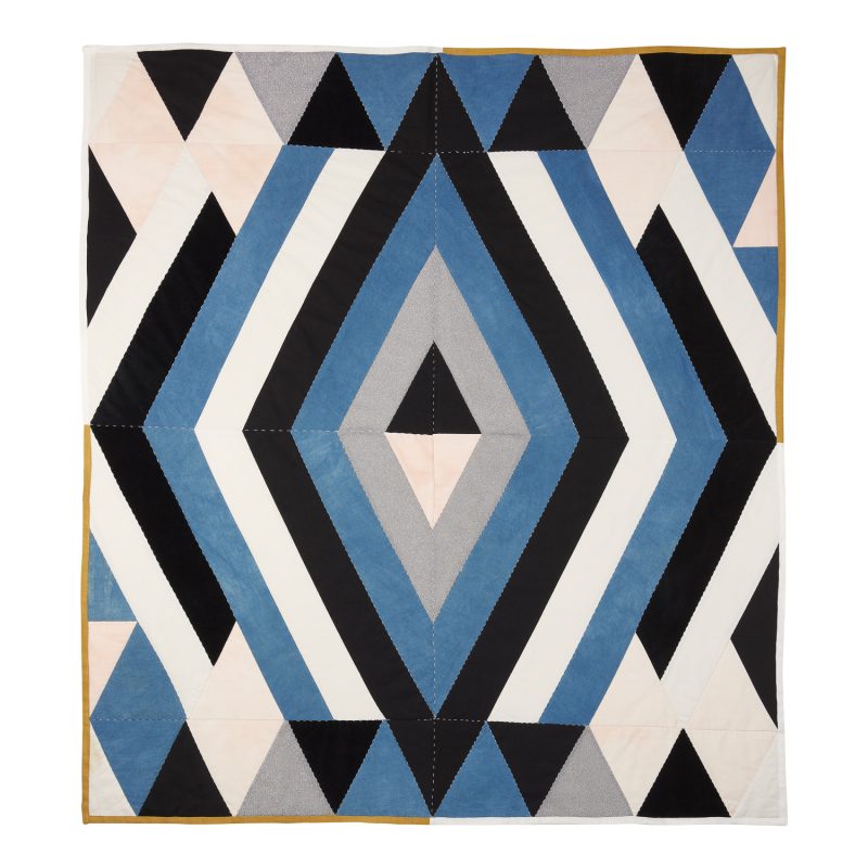 a quilted hand dyed quilt hanging from a bar. its main colour is blue and within that colour are organic abstract shapes in pale pink, creamy white and a taupe.