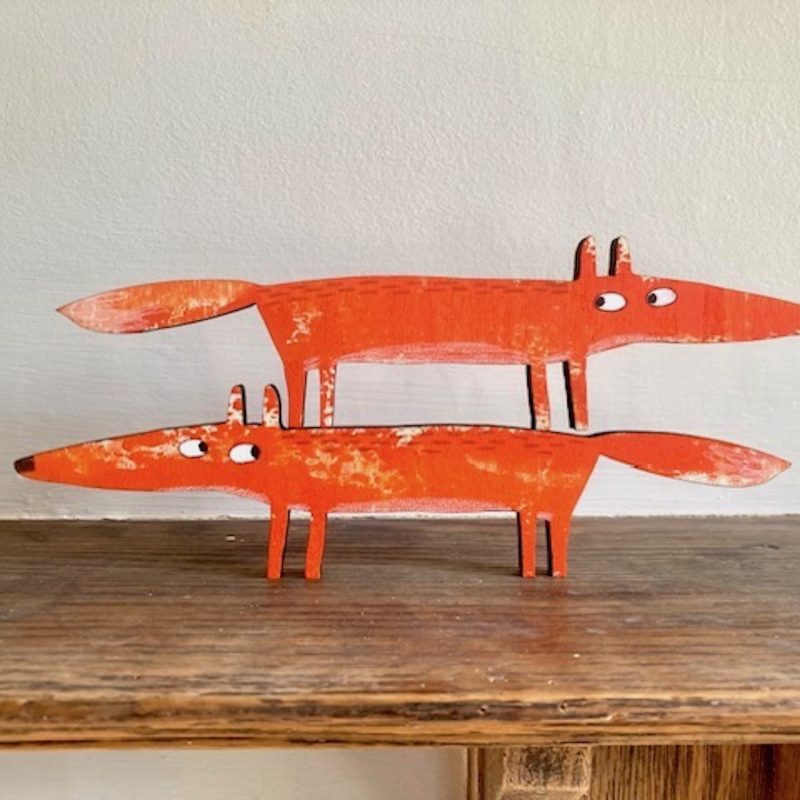 The image shows two hand printed freestanding wooden foxes, standing on top of each other.
