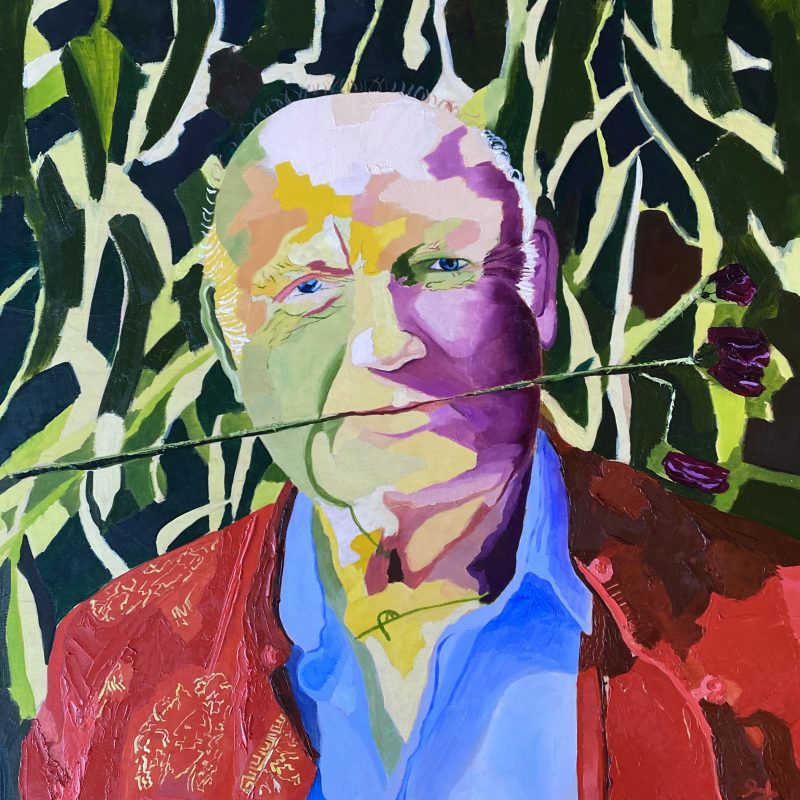 This is a portrait of Louis de Bernieres. He has a flower in his mouth, and his cheeks are painted purple and green. The background is covered in greenery