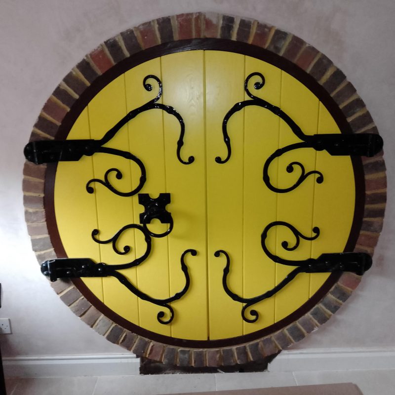 Yellow circular door with decorative metal work hinges and knocker