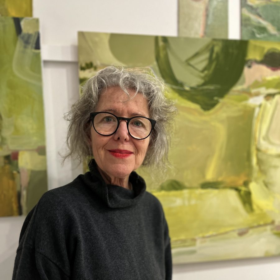 Head and shoulder portrait of Artist Jo Watters-Pawlowksi in her studio standing in front of one of her paintings.  The painting is a work in progress,  inspired by the South Downs.