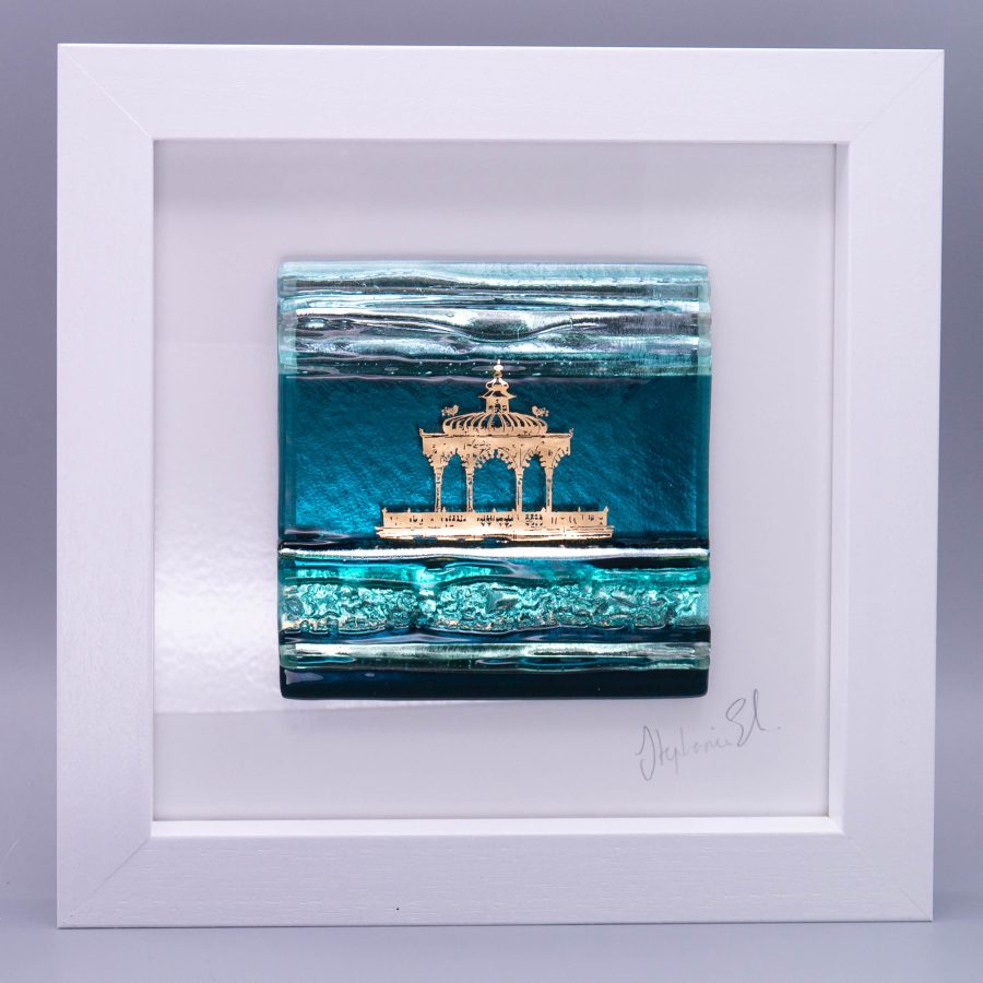A textured glass tile in shades of teal and silver glass with an abstract image of Brighton Bandstand in shiny 22ct gold
