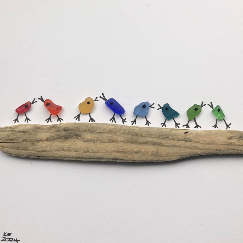 Eight pieces of coloured Scottish sea glass in shades of red, orange , yellow blue and green arranged as birds sat chattering on a piece of driftwood.
