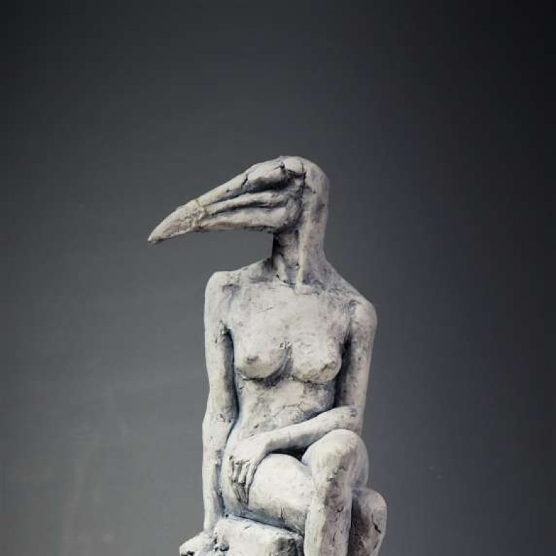 A porcelain sculpture of a women with a birds head, sat on on a tall pillar