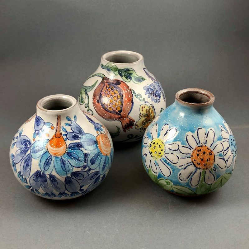 A group of three round bud vases wheel thrown in red terracotta clay, decorated with tin white glaze and brightly coloured floral on-glaze designs. 