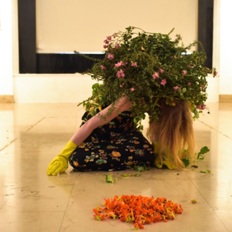 Woman bent over on the floor wearing marigold gloves and covered in foliage
