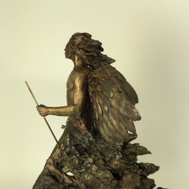 Small bronze sculpture of a male skirted figure strides forward holding a staff.