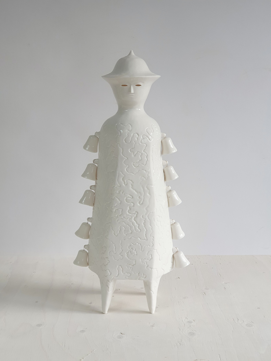 White porcelain sculpture in abstract human form with a hat and bells running down the side.Textural and beautifully made.