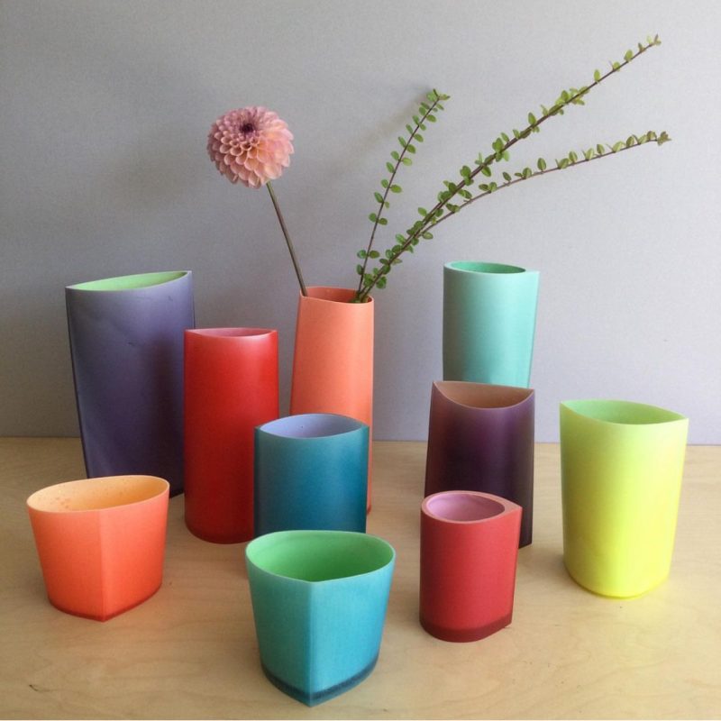 a collection of brightly coloured resin vessels sitting close together. on vessel at the back has a pink chrysanthemum.