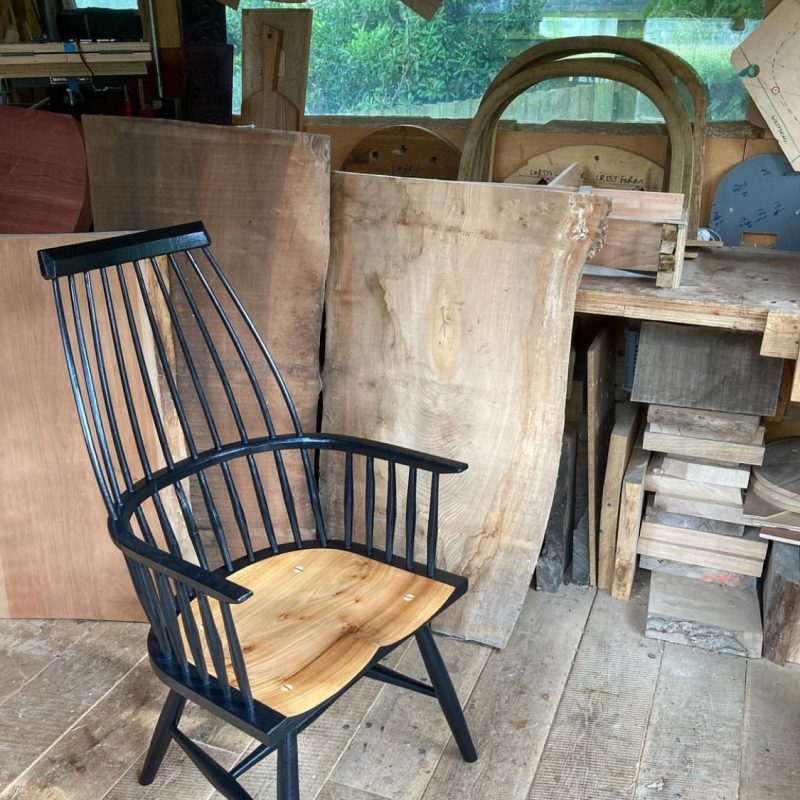 Hopesprings Chairs workshop showing a high backed chair in natural wood and black painted details surrounded by larger blocks of wood.