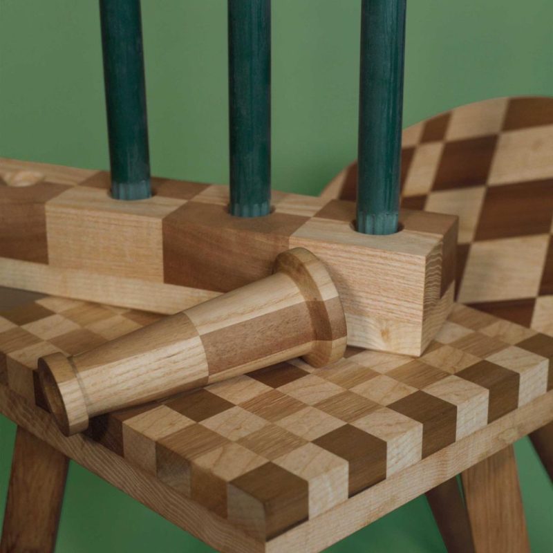 close up image of checkerboard stool seat with a collection of candlesticks against a green background.