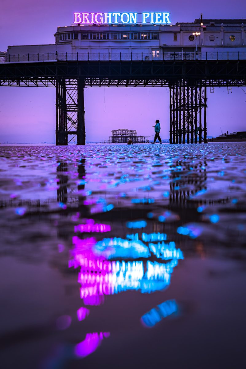 Purple lights reflected from Brighton Pier on a low tide beach at night 