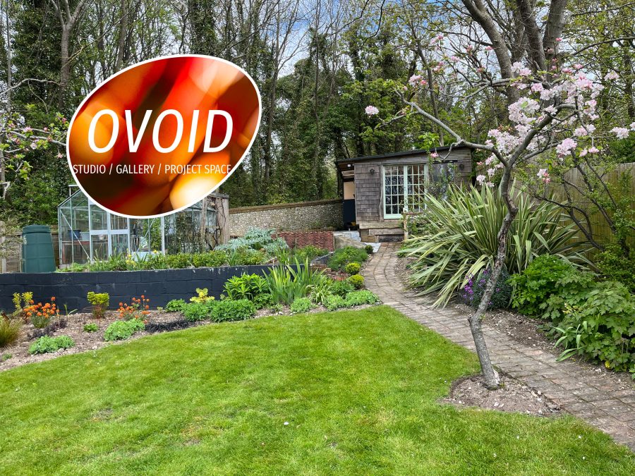A photo of a shed at the top of a garden with woods behind and vegetable beds in front. An egg shaped logo with the words 
