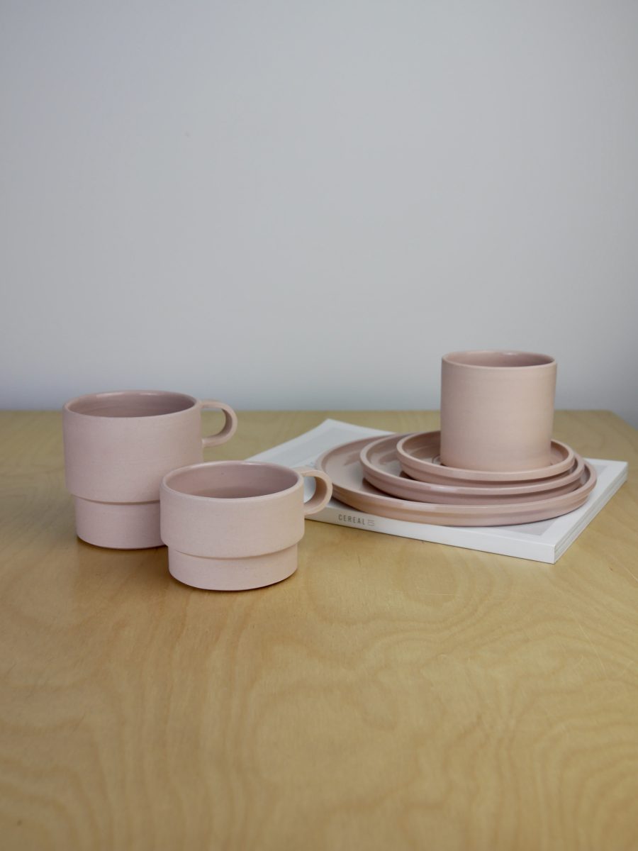 A collection a tableware in blush pink. Tumbler placed on top of saucer, which is stacked onto small plate and medium plate. Tall angular mug and short angular mug positioned on the left of the image.  