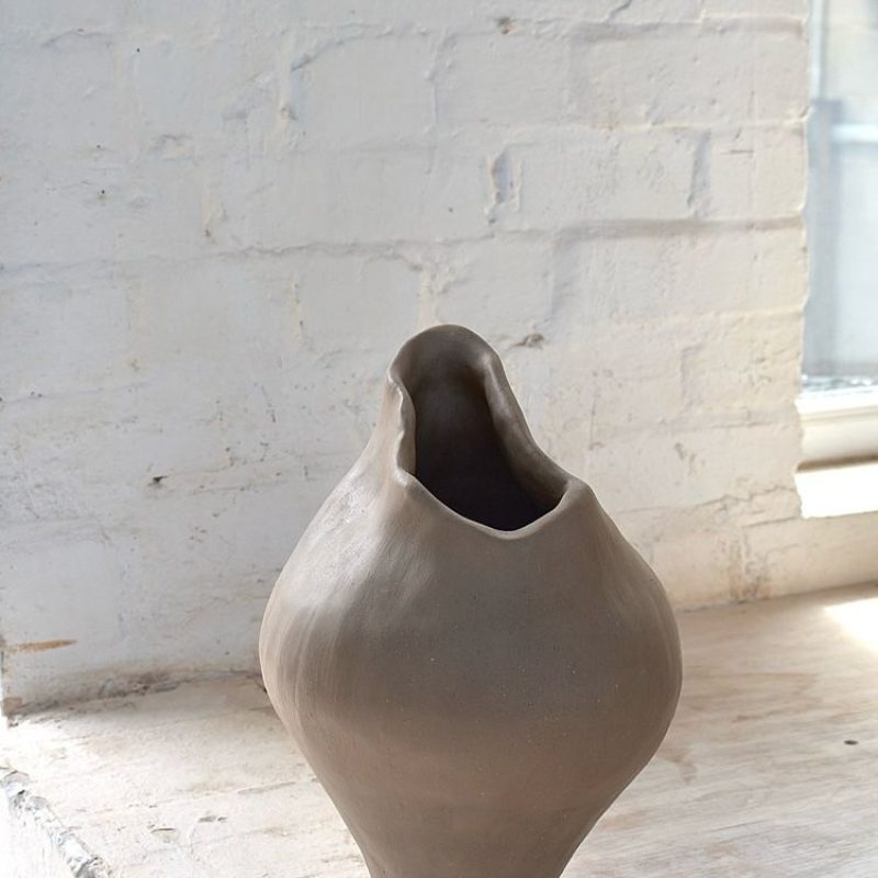 Sculptutral vessel that is a representation of the human form, standing on a thin base as it curves out into a wide body before curving into the top with a slanting rim bringing the eice together.