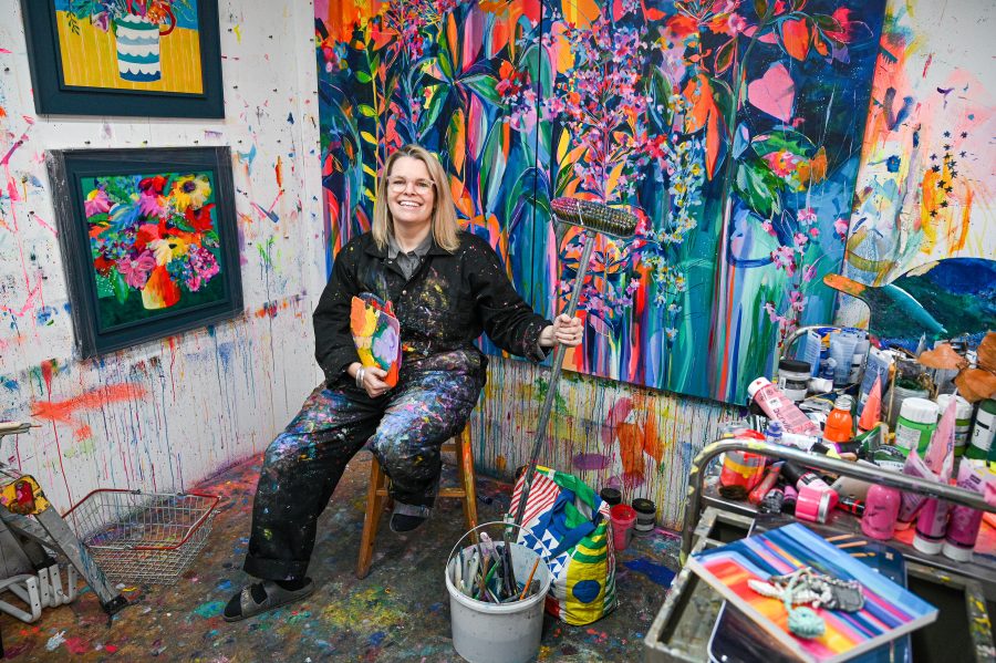 Faye Bridgwater in her studio holding a broom with a large floral painting behind