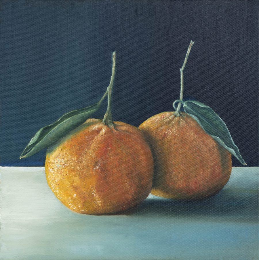 Two clementines with stalks and leaves, on a table surface