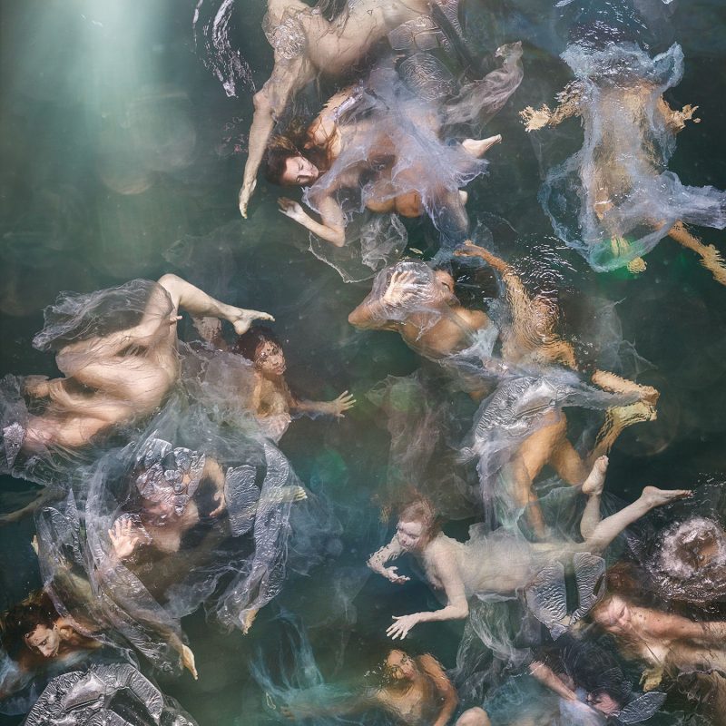 A photograph showing a large group of nude women in the water. The women are partly submerged and are tangled in sheer sheets of plastic. The image has a baroque feel and is inspired by heavenly scenes in 18th century ceiling frescos.