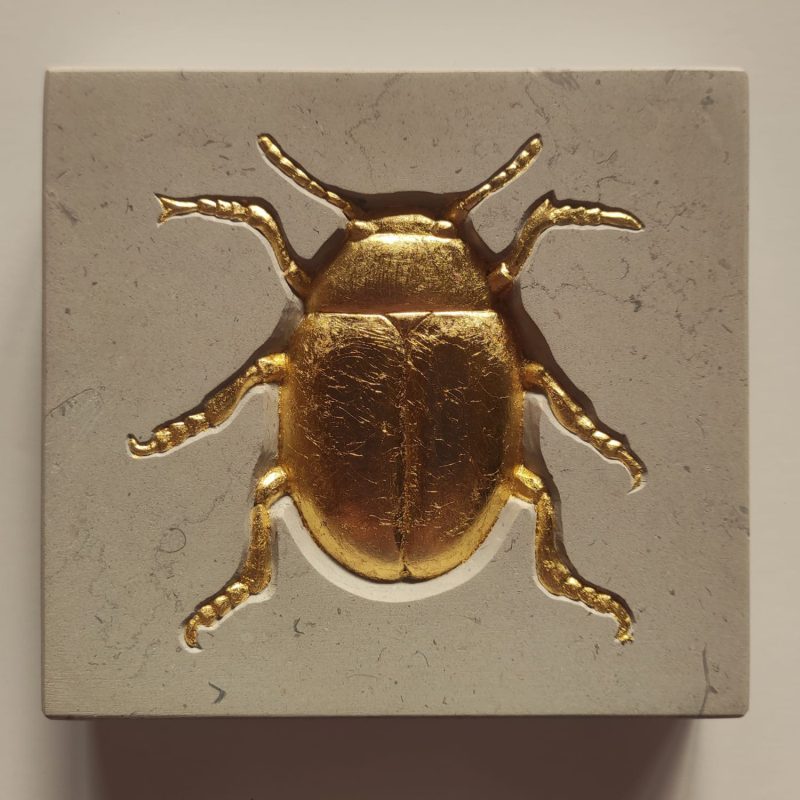 An anatomical study of a Colorado Potato Beetle relief carved into French limestone and highlighted in gold leaf.